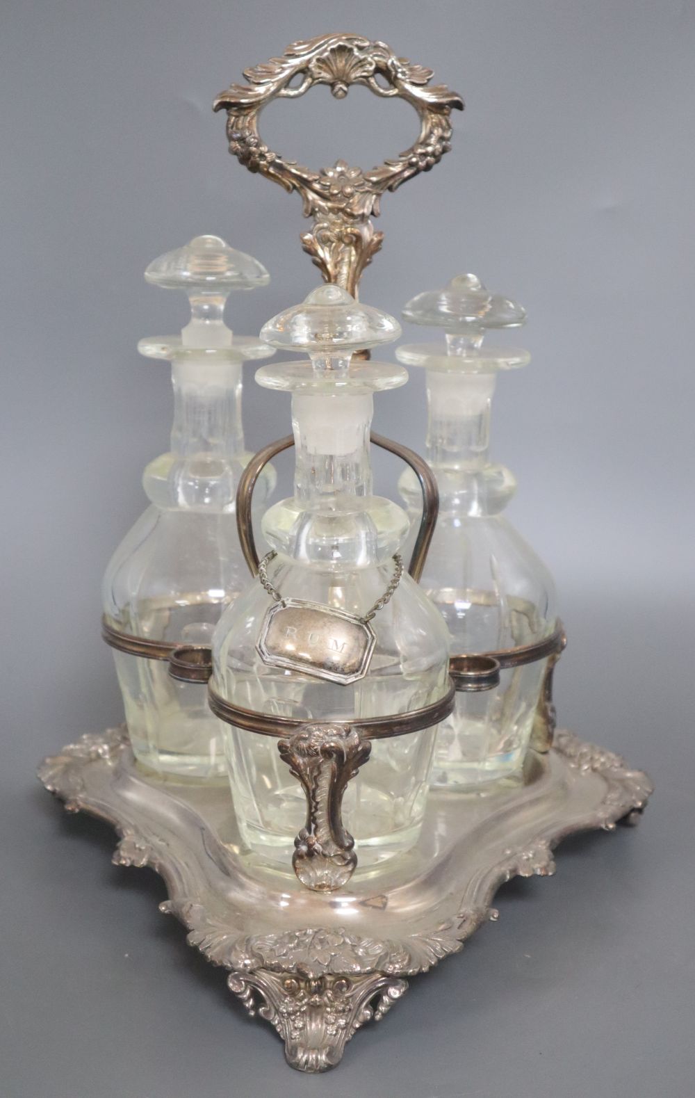 A plated three decanter tantalus of triangular form with leaf-wrapped handle, with bottles and stoppers, height 38cm